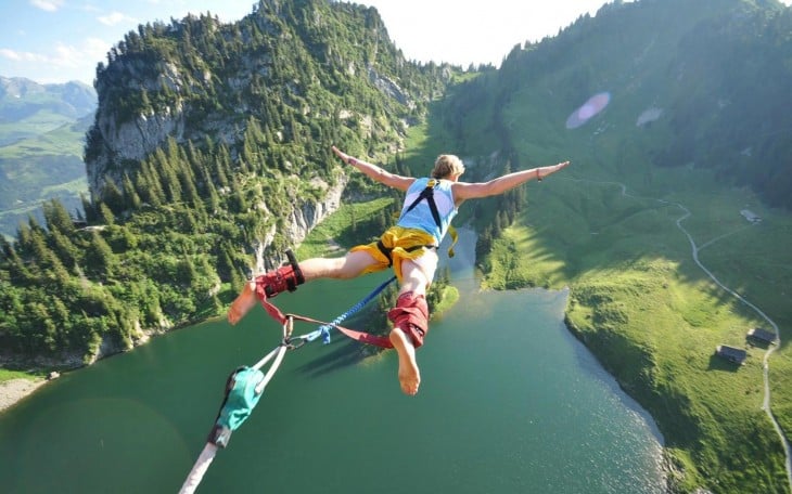 hombre saltando del bungee en un lago y montañas