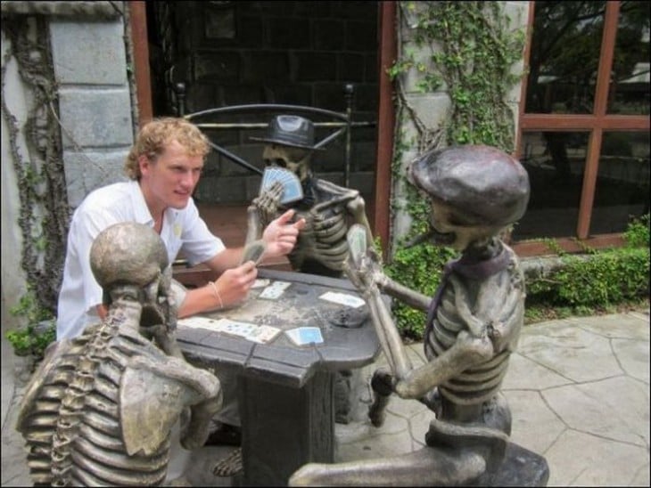 hombre jugando cartas con estatuas de calaveras