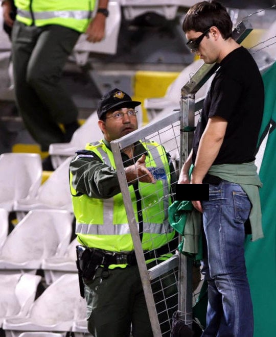 hombre orinando en gradas de estadio con policia a un lado