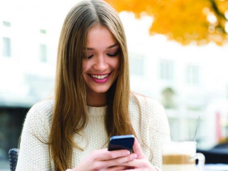 Chica sonriente escribiendo en su teléfono