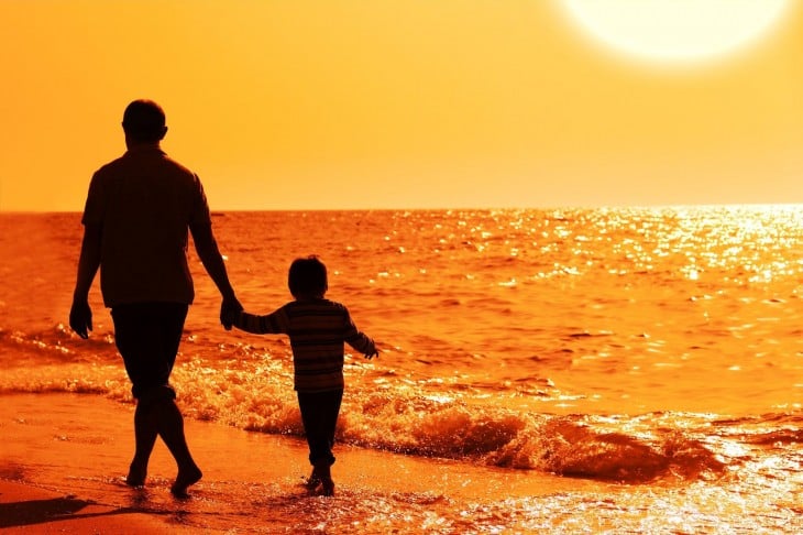 Padre e hijo caminan en la playa al atardecer