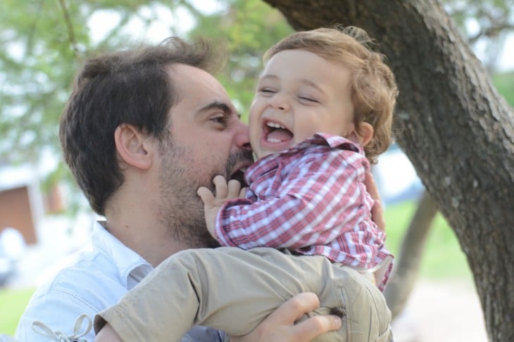 Niño ríe al jugar con su padre