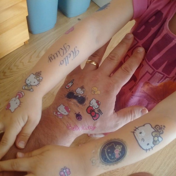 mano de un hombre con tatuajes de hello kitty en medio de los brazos de su hija 