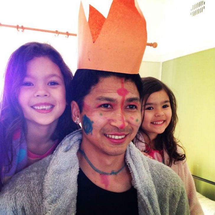 hombre en medio de sus dos hijas pintado de la cara y con una corona de papel en su cabeza 