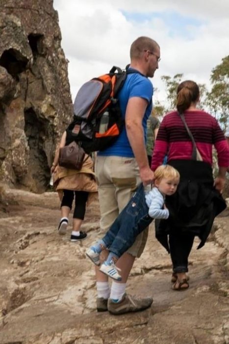 papá cargando a bebé de los tirantes con overol