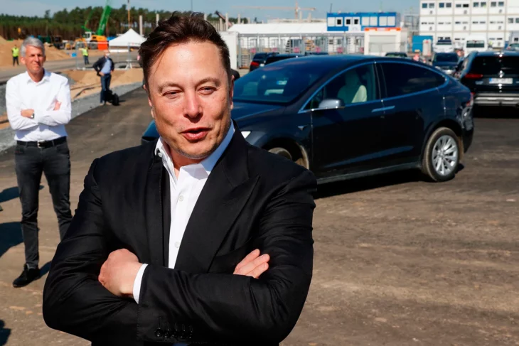 Elon Musk de brazos cruzados frente a tesla y compinche igualmente posando