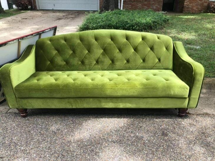 sofá de terciopelo color verde en la acera de una calle 