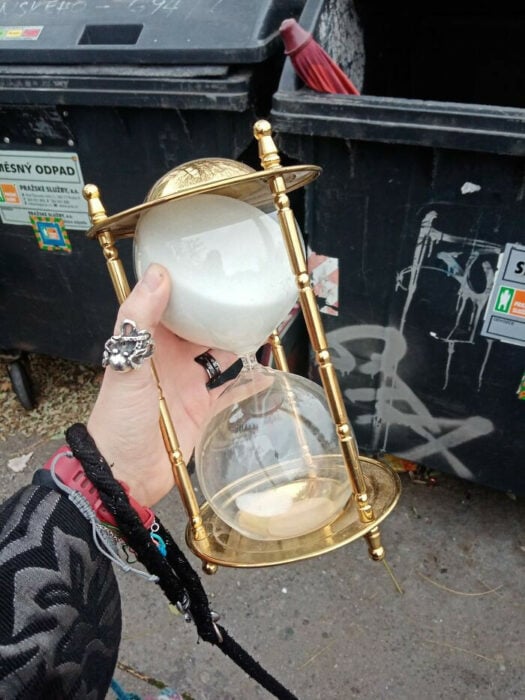 mano con un reloj de arena antiguo frente a un contenedor de basura