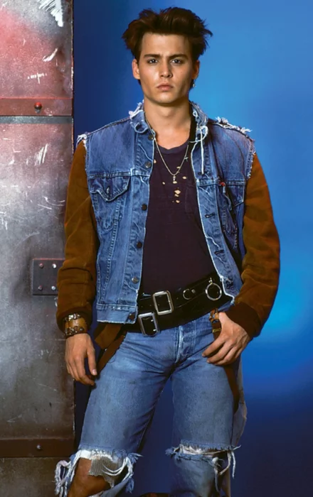 Johnny Depp en mezclilla y chaleco mano akimbo apoyándose en una puerta metálica su personaje de 21 jump street