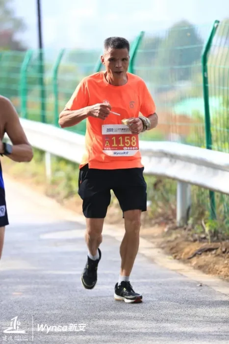 El Tío Chen un maratonista chino con el número 1158 de la maratón se dispone a fumar otro cigarrillo durante la carrera va con camisa naranja y pantaloncillo negro