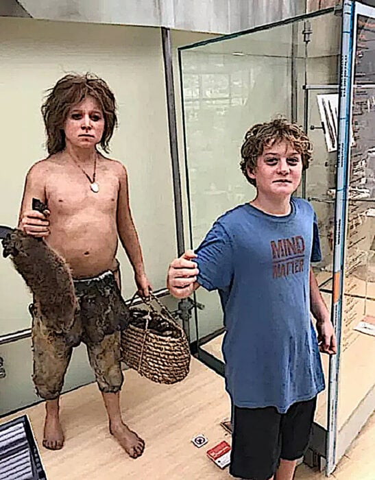 Drew chico con camiza azul se compara con una figura de un joven prehistórico en el museo de ciencia de trento en Italia