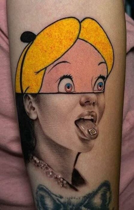 Tatuaje de alicia en el país de las maravillas de disney que muestra la mitad del rostro de alicia caritcaturizado y la otra mitad realista mientras consume una estampita con ácido sustancia narcótico que la hace alucinar