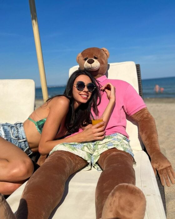 mujer acurrucándose en la playa en su Loving Bear Puffy en sillas de playa ella en top verde y oso en pantalones cortos y camisa rosa