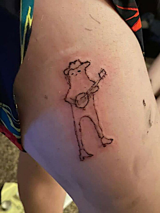 Un tatuaje de un bicho probablmente un sapo tocando el banjo