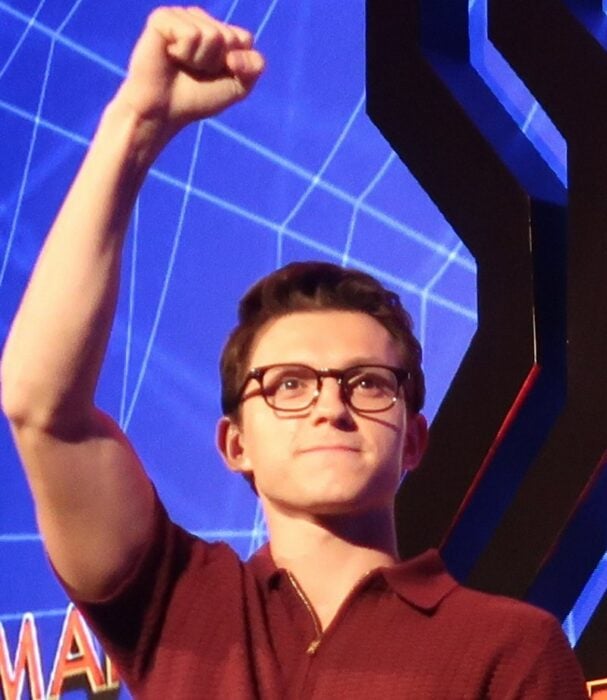 TOm Holland con camisa roja y con lentes levantando el puño en la presentación de SPider-Man
