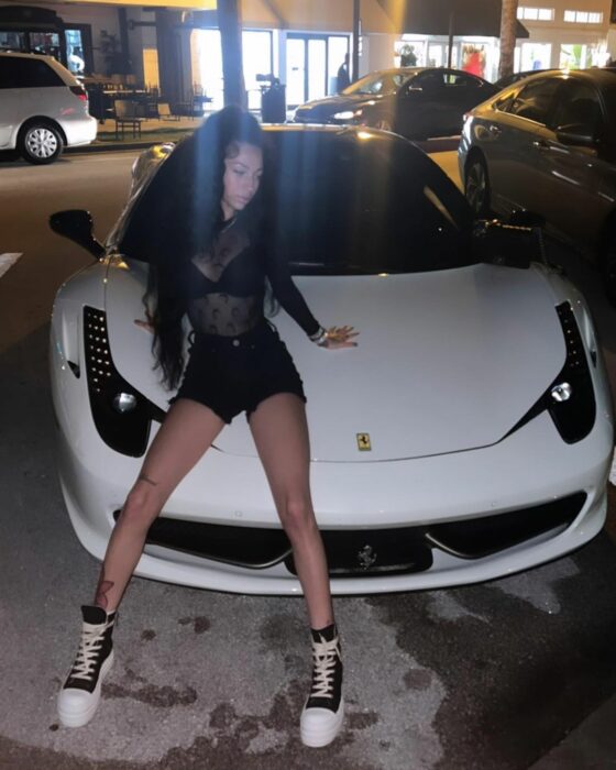 Bhad Bhabie sobre un Ferrari blanco vestida de negro pantalon corto tenis negros