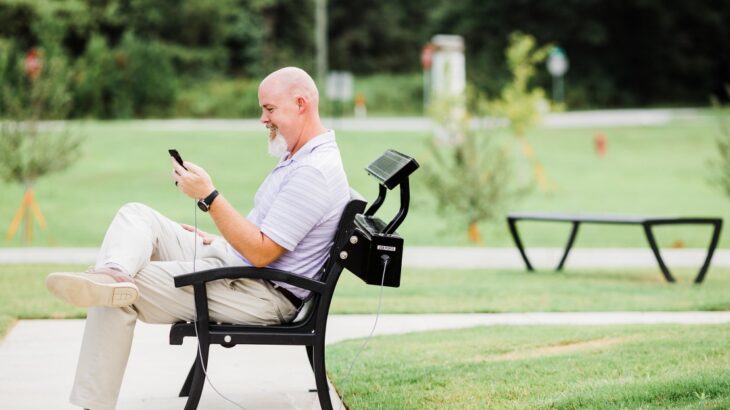 Cargador de USB solar integrado a una banca de parque un hombre carga su teléfono