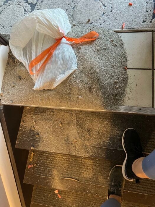 una bolsa rellena de arena de sus mascotas gatos perros litterbox desparramándose en las escaleras y en los zapatos de la dueña