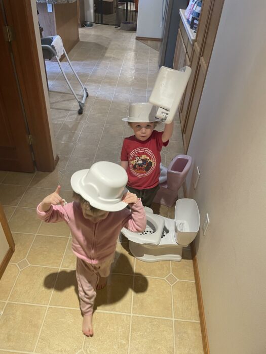dos niños que están siendo entrenados para ir al baño utilizan las bacinicas como sombreros