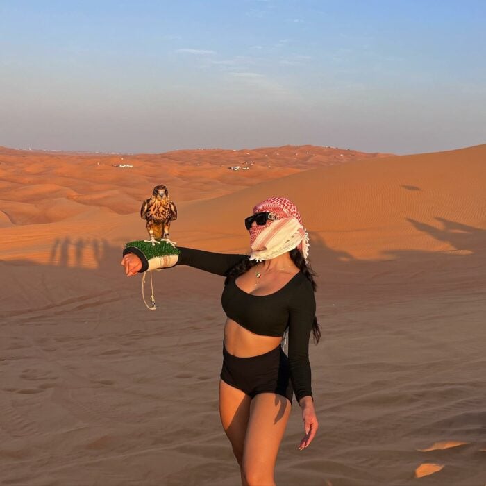 Jenny Martínez en el desierto con la cabeza cubierta cetrería halcón en brazo lentes oscuros top deportivo negro pantaloncillo negro