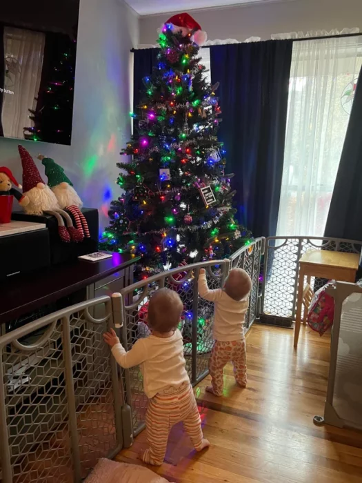 Dos bebés contenidos por un corral para vitar que echen a perder un árbol de navidad