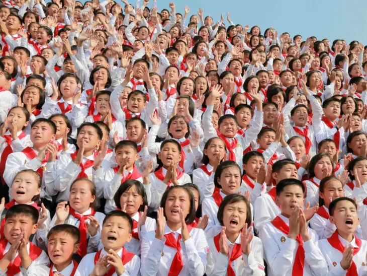 Niños norcoreanos en una reunión multitudinaria con uniformes blancos con listones rojos, aparentemente gritando