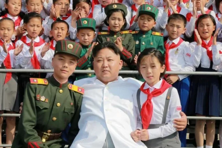 Kim Jong-un vestido de blanco líder de Corea del Norte abrazando a una niña y a un militar en una reunión multitudinaria 