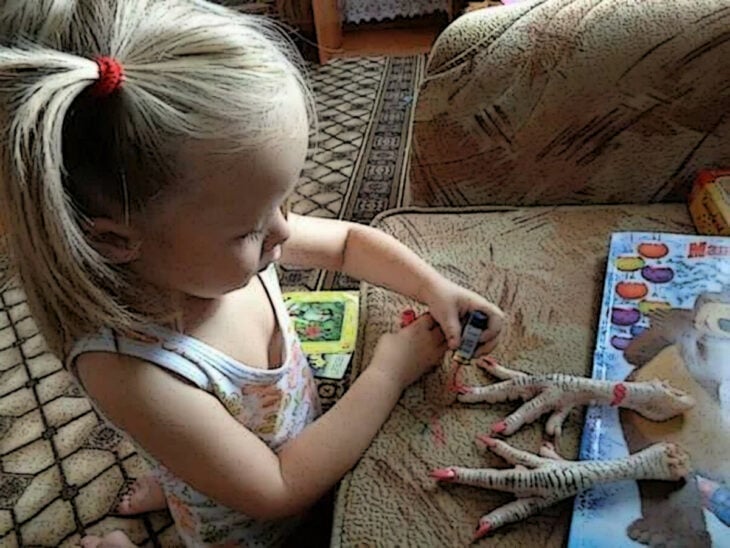 Niña pintándole las uñas a unas patas de pollo