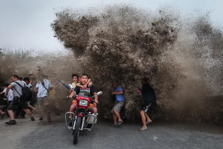 Hombre en motoneta con familia esquivando una ola que rompe detrás de ellos