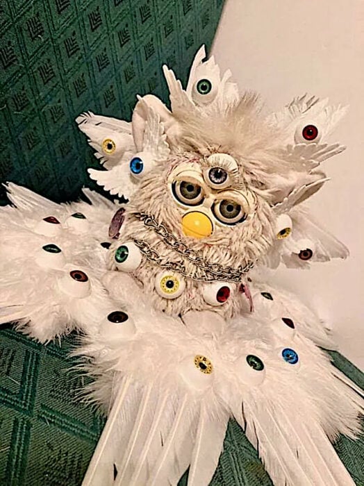 Furby angelical con plumas y ojos extra imitando a ángeles antiguos