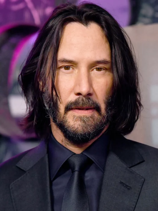 Keanu Reeves de traje negro y camisa oscura barba bigote