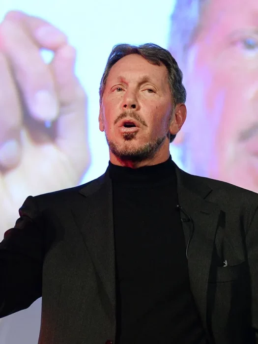 Larry Ellison en conferencia traje negro y su proyección a sus espaldas