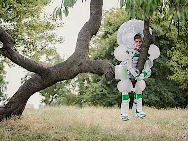 Niño sobre la rama de un árbol viste un traje extraño que parece inspirado en la era espacial probablemente un traje de seguridad plástico Regreso del niño burbuja