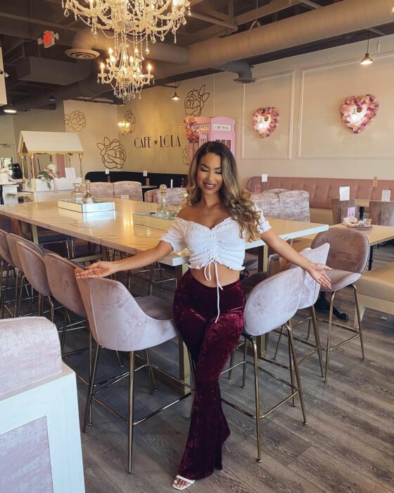 SHye Lee influencer blusa blanca pantalón guinda en salón de fiestas restaurante con brazos abiertos