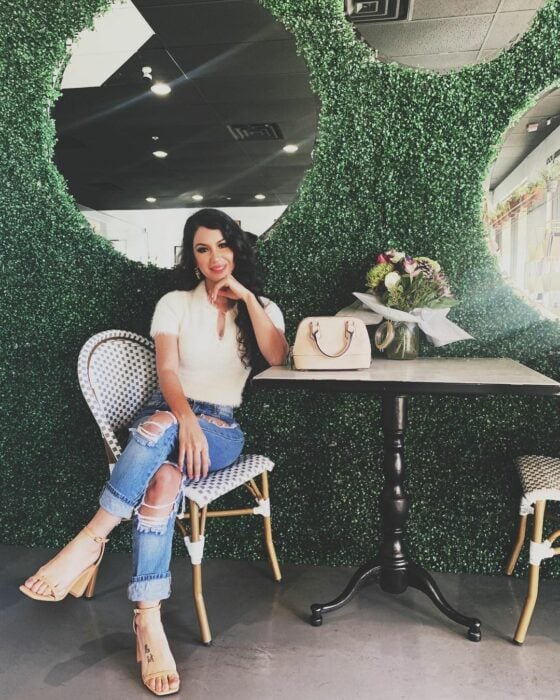 Shye Lee sentada en un café influencer tiktoker pantalones de mezclilla rasgados y top blanco bolso y huaraches sandalias blancas