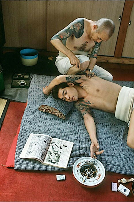 Yakuza recibiendo su tatuaje mientras fuma un cigarrillo y lee un manga