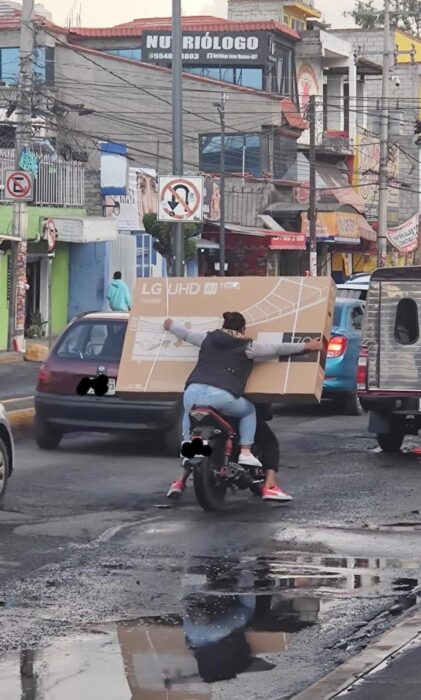 Mujer cargando televisión en moto